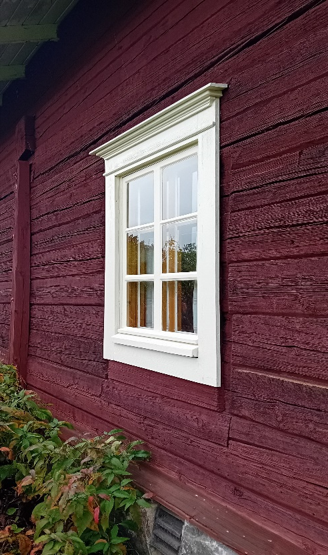 Valkoisilla karmeilla koristeltu ikkuna puutalon seinässä